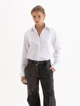 Camisa de algodón con lycra, de corte clásico y manga larga. Presenta cierre frontal con cartera oculta, puños abotonados y apliques de piedras cristal en las puntas del cuello.