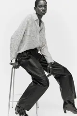 Camisa de manga larga con cuello camisero y cierre frontal de botones. Presenta un estampado geométrico en blanco roto y negro, compuesto por líneas rectas y curvas que forman patrones abstractos.