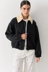 Campera bomber de paño negro con cuello de piel sintética desmontable en color crema. Presenta cierre frontal, puños y ruedo elásticos, con un diseño de corte holgado.