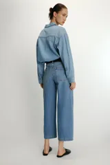 Camisa de denim de corte oversize con cuello solapa, manga larga con puños, cierre frontal con botones a presión y bolsillos de plastrón en el delantero.