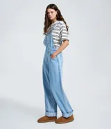 Peto de jean azul claro con corte recto, escote cuadrado, tirantes ajustables con hebillas metálicas y cierre lateral con botones. Cuenta con bolsillo frontal tipo parche y bolsillos laterales funcionales.