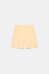 Bermudas color amarillo claro de tiro alto con bolsillos laterales ocultos en costura, detalle de pinzas en delantero y cierre frontal con cremallera y ganchos metálicos.