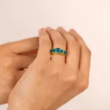 Anillo dorado con cinco piedras rectangulares de color azul.