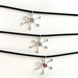 Gargantilla con dije de plata 950 en forma de sol con piedra roja en el centro, atada con tiento color beige.