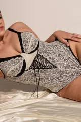 Body de lycra y puntilla elastizada color crudo con detalles en negro. Tiene aro, breteles regulables y detalle de cintas cruzadas en el frente.