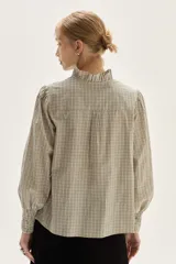 Blusa de algodón con estampado de rayas verticales en tonos crudo y negro. Presenta cuello mao con lazo para atar, bordados florales en negro y beige en la zona del pecho y hombros, y mangas largas con puños fruncidos elásticos.