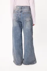 Jean de corte wide leg en denim azul claro con efecto lavado. Presenta bordados del logo de la marca en color ocre en ambos laterales a la altura de las rodillas y ruedo desflecado.