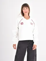 Buzo azul oscuro de corte holgado con cuello polo y escote en V. Presenta mangas largas con costuras raglán en color blanco y un estampado frontal con la palabra Ambience y el texto United Nation League en tonos dorados.