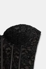 Corsé de encaje negro con escote corazón, hombros descubiertos y varillas interiores para estructura. Cuenta con cierre lateral mediante cremallera oculta.