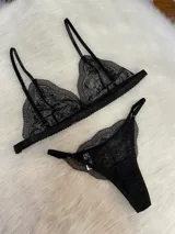 Conjunto de lencería de tres piezas en encaje negro. Incluye bralette con breteles regulables y collarín integrado, y tanga regulable con corte media less.