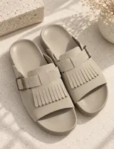 Sandalia beige con capellada de ante, diseño de flecos frontales y tira ajustable con hebilla metálica lateral.
