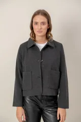 Chaqueta de paño color gris oscuro, con cuello camisero, cierre frontal de botones y dos bolsillos frontales tipo parche. Presenta un corte recto y mangas largas.