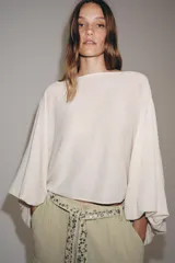 Cuerpo de punto color crudo, con cuello barco y mangas largas abullonadas con sisa ancha y puños ajustados.