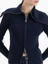 Cardigan de tejido de punto fino con silueta ajustada, cuello alto y cierre frontal de doble camino. Presenta mangas largas con aberturas para los pulgares.