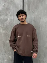 Buzo marrón con logo "Osten" y diseño gráfico de sol en color beige. Corte oversize, cuello redondo y mangas largas.