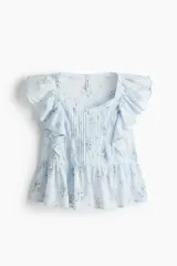 Top de algodón color celeste con estampado floreado, escote corazón y mangas con volados. Presenta detalles de jaretas frontales y corte peplum con vuelo en la parte inferior.