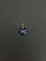 Dije de forma circular con diseño floral tallado en piedra natural azul, engastado en metal dorado con una circonia central.