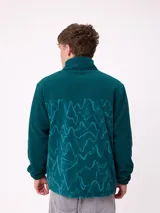 Campera reversible con cuello alto y cierre frontal. Un lado presenta tejido de polar con estampado geométrico en tonos verdes y bolsillo con cierre en el pecho, mientras que el otro lado es de nylon. Cuenta con puños elásticos y bolsillos laterales.