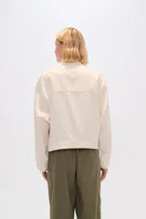 Chaqueta color crema de algodón con cuello mao, cierre frontal con botones, bolsillos laterales y mangas largas.