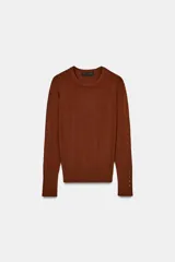 Jersey de punto liso color negro, con cuello redondo y manga larga. Presenta una hilera de cuatro botones dorados decorativos en el puño de cada manga.