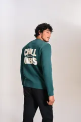 Buzo verde oscuro de cuello redondo, mangas largas con puños elásticos y pequeño estampado ovalado en el pecho.