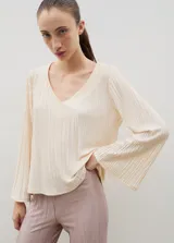 Blusa plisada de color crema con escote en V y mangas largas ligeramente acampanadas. Presenta una textura plisada en toda la prenda que aporta caída y movimiento.