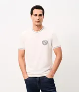 Remera de manga corta y cuello redondo color blanco crudo, con detalles de ribetes oscuros en cuello, mangas y ruedo, y un pequeño escudo bordado en el pecho.