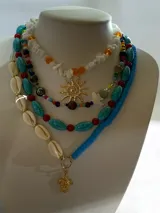 Collar de cuentas asimétrico compuesto por piezas alargadas de imitación piedra turquesa con vetas negras, intercaladas con pequeñas cuentas esféricas de color rojo. Incluye cadena extensora metálica en tono dorado.