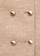 Chaqueta de tweed en color beige con diseño recto, cuello redondo y cierre frontal de doble botonadura con botones dorados. Presenta dos bolsillos de parche en el pecho y forro interior.