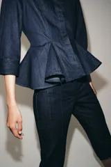 Pantalón capri de tiro medio confeccionado en denim de algodón. Presenta bolsillos de vivo en el delantero, cierre frontal con cremallera, botón y ganchos metálicos, y aberturas laterales en el bajo.