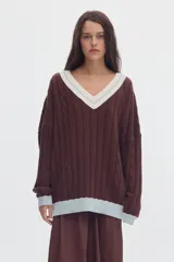 Sweater de punto oversized de color marrón, con escote en V, detalles de ochos y puños, cuello y ruedo en tono celeste y blanco.