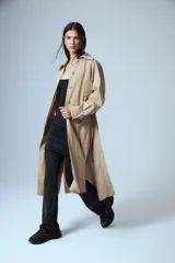 Trench midi de color camel, confeccionado en una mezcla de algodón y nylon con propiedades repelentes al agua. Presenta un diseño clásico con cuello camisero, cierre frontal de botones, bolsillos laterales y tajos en los costados.