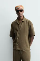 Camisa de corte relajado confeccionada en lino color verde militar, con cuello solapa, manga corta y cierre frontal de botones.