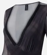Body de tul negro con transparencia, manga larga y escote en V profundo con detalle de encaje en el borde. Presenta un diseño ajustado al cuerpo con cierre de broches a presión en la parte inferior.