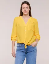 Blusa de calce relajado color salmón, confeccionada en tela liviana con textura sutil. Presenta escote en V con abotonadura frontal, bolsillo parche en el pecho, mangas largas regulables con presilla y ruedo con opción de anudar en el frente.