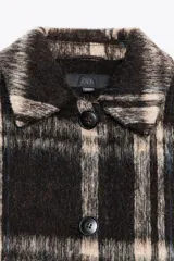 Chaqueta de corte recto con cuello solapa y cierre frontal de botones. Presenta un diseño de cuadros en tonos oscuros y beige con textura de lana.