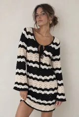 Vestido corto de punto calado con patrón de rayas onduladas en color negro, blanco y beige, de manga larga y escote en V con cordones para atar.
