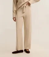 Pantalón wide leg de punto color beige, de tiro medio con cintura elástica ancha de rib, lazo ajustable con punteras metalizadas y costuras verticales decorativas.