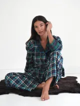 Pijama de franela a cuadros con estampado tartán, compuesto por una camisa de manga larga con solapas, bolsillo frontal y botones, y un pantalón largo de corte recto con puños y detalles en verde.