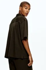 Camisa de manga corta H&M con cuello abierto, confeccionada en tejido de punto con textura. Presenta un diseño de corte holgado con bajo recto y aberturas laterales.