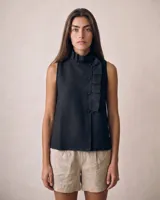 Blusa sin mangas de lino color negro, con cuello alto plisado, cierre lateral asimétrico con botones forrados y detalles de pliegues frontales.