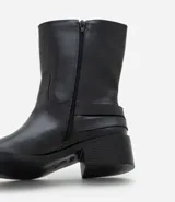 Bota de caña corta marca Satinato, confeccionada en poliuretano color negro. Presenta punta redondeada, taco bloque bajo y dos tiras decorativas con hebillas metálicas en el lateral externo.