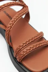 Sandalias color marrón con tiras trenzadas y ajuste de velcro en el talón. Plataforma de 3cm de alto y suela negra.