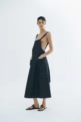 Vestido midi de denim color azul oscuro, confeccionado con mezcla de algodón. Presenta escote cuadrado, tirantes anchos, bolsillos delanteros de parche y falda de corte evasé.