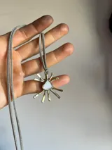 Gargantilla con cordón de gamuza gris y dije de sol dorado con centro de nácar.