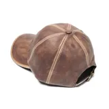 Gorra tipo béisbol confeccionada en cuero sintético color marrón con efecto desgastado y costuras decorativas en contraste.