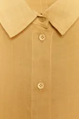 Camisa de color mostaza, con cuello solapa, manga corta y bajo recto. Cierre frontal con botones.