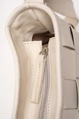 Cartera tipo morral de cuero color beige, con diseño trenzado artesanal, correa larga regulable y cierre superior.