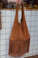 Maxi cartera tipo bolso de cuero gamuza natural color tostado, con flecos colgantes en toda su base y diseño blando sin forro.