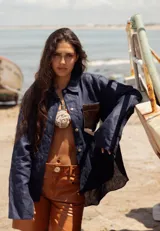 Camisa color naranja de lino o algodón con cuello clásico, cierre frontal con botones y mangas largas con puños abotonados. Presenta un bolsillo de cuero marrón en el pecho.